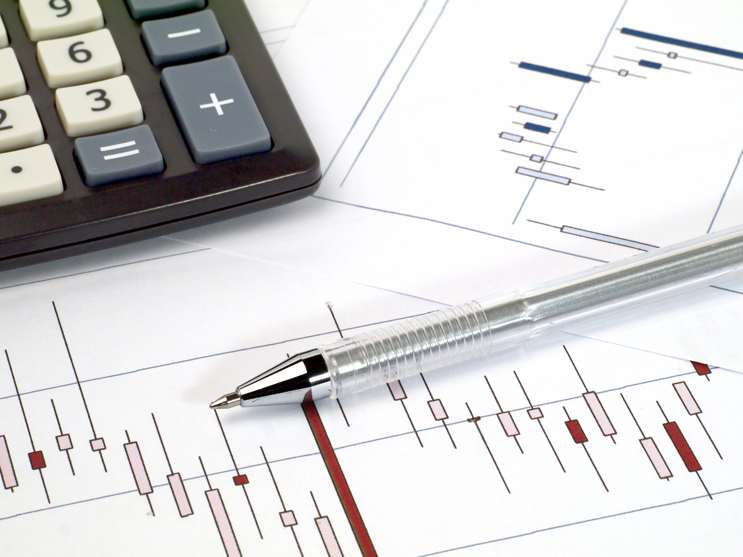 ballpoint pen and calculator on printed candlestick charts